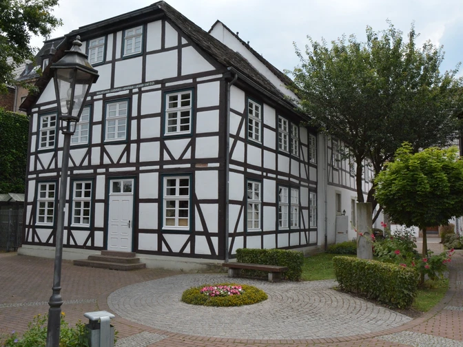 Haus des Gastes Fachwerkhaus mit weißen Wänden und dunklen Holzbalken, umgeben von gepflegten Grünanlagen.