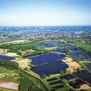 Naturschutzgebiet Rietberger Fischteiche Luftaufnahme von zahlreichen blauen Teichen in einer ländlichen, grünen Landschaft mit Kleinstadt im Hintergrund.