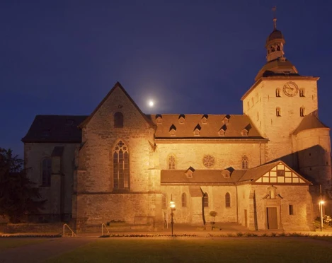 Eggeedom Neuenheerse Neuenheerse: Historische Steinkirche bei Nacht, angestrahlt, mit Uhrturm und beleuchteten Fenstern.