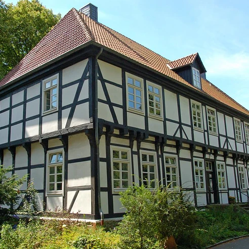 Herrenhaus in Stift Quernheim Das Herrenhaus in Stift Quernheim aus Fachwerk steht inmitten einer grünen Umgebung neben Bäumen.