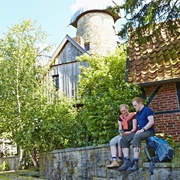 Levedags Mühle: Rast Ein Paar sitzt auf einer Steinmauer vor der historischen Levedags Mühle, umgeben von grüner Natur.