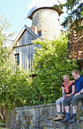 Levedags Mühle: Rast Ein Paar sitzt auf einer Steinmauer vor der historischen Levedags Mühle, umgeben von grüner Natur.