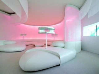 Futuristisch gestalteter Raum mit weißen, geschwungenen Sitzmöbeln und sanfter rosa Beleuchtung.