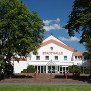 Stadthalle Brakel Große weiße Stadthalle mit rotem Schriftzug, umgeben von Bäumen, unter blauem Himmel.