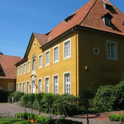 Hilter - Rathaus Gelbes Rathausgebäude mit roten Ziegeldächern, umgeben von gepflegten Sträuchern und Bäumen.
