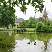 Teich im Garten der Klosteranlage Herzebrock Ruhiger Teich mit Enten im Vordergrund, alte Kirche und gepflegte Gärten im Hintergrund.