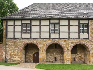 Historisches Fachwerkhaus mit Steinmauer, drei Rundbogenportalen und teilweise bewölktem Himmel.