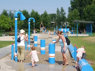 Ein Wasserspielplatz mit blauen Röhren, Kindern und Erwachsenen beim Spielen und Erkunden im Freien.