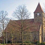 Steinernen Kirche Kirchlengern mit rotem Dach, Glockenturm und kahlen Bäumen im Vordergrund.