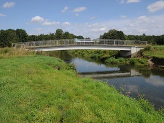 Alte Else - neue Else Eine moderne Stahlbrücke überquert einen ruhigen Fluss in einer grünen, von Bäumen gesäumten Landschaft.