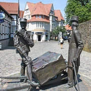 Bronzeskulptur von zwei Männern mit Pferdekarren auf Kopfsteinpflasterstraße im urbanen Umfeld.