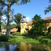 Gut Böckel Schloss Gut Böckel mit gelben Wänden und einem Turm inmitten grüner Bäume reflektiert im Wasser.