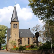 Historische Michaelkirche aus Backstein mit hohem Turm, umgeben von Bäumen und gepflegtem Garten.
