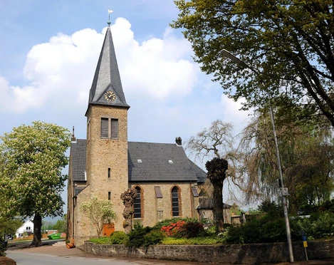 Historische Michaelkirche aus Backstein mit hohem Turm, umgeben von Bäumen und gepflegtem Garten.