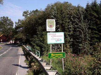 Straßenschild an der Grenze zwischen Niedersachsen und Nordrhein-Westfalen bei Warmenau, umgeben von Bäumen.