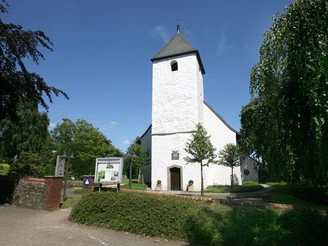 Autobahnkirche Exter Weiße Autobahnkirche Exter mit quadratischem Turm, umgeben von grünem Laub vor blauem Himmel.