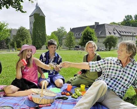 Picknick im Schlosspark Brakel-Gehrden Eine Familie genießt bei Sonnenschein ein Picknick auf einer Wiese vor einem historischen Schloss.