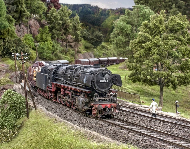 Modellbundesbahn Dampflokomotive Baureihe 44 Dampflokomotive der Baureihe 44 fährt durch eine modellierte Landschaft mit Bäumen und Hügeln.
