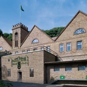 Barres Brauwelt Außenansicht Historisches Backsteingebäude mit Zinnengiebel und Brauereilogos, umgeben von bewaldeter Landschaft.