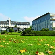 Klinik Dreizehnlinden Große Grünfläche mit herbstlichen Blättern, dahinter zwei moderne Gebäude der Klinik Dreizehnlinden.