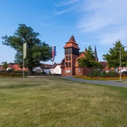 Historisches Gebäudeensemble mit einem zentralen, hohen Turm, umgeben von Rasen und blühenden Gärten.