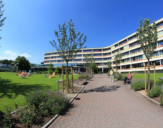 Knappschafts-Klinik Bad Driburg Moderner Klinikbau mit gepflegter Gartenanlage, Sonnenschirmen und Liegestühlen, klarer Himmel.