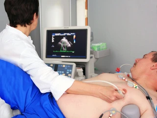 Diagnostik Ein Arzt führt eine Ultraschalluntersuchung des Herzens bei einem liegenden Patienten durch.