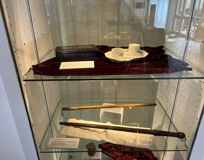 Dauerausstellung Susanna Abraham Kunstvoll arrangierte Ausstellungsstücke in einer Vitrine, darunter Teetassen und historische Accessoires.