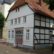 Storchenhaus in NRÜ Außenansicht Fachwerkhaus mit rotem Ziegeldach und weißen Fenstern, teils verschattet unter blauem Himmel.