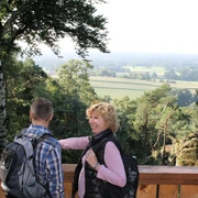 Blick von der Aussichtsplattform an der Almhütte Zwei Wanderer genießen den weiten Blick über Wälder und Felder von einer hölzernen Plattform.