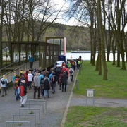 Info-Box am Naxxen Dreieck in Hörstel Eine Gruppe von Wanderern gelangt über einen schmalen Gehweg zu einer überdachten Info-Box am See.