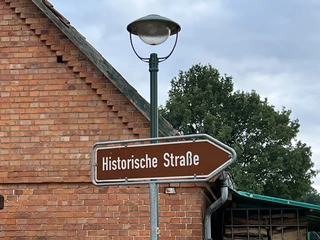 Historische Straße Altes Straßenschild mit der Aufschrift "Historische Straße" vor einer Ziegelmauer und Bäumen.