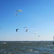 kiten-mardorf Kitesurfer gleiten an einem sonnigen Tag über das Wasser, prächtige Drachen tanzen am klaren Himmel.