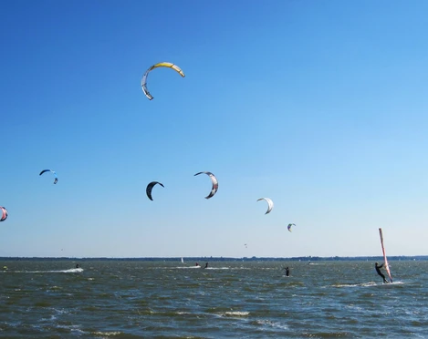 kiten-mardorf Kitesurfer gleiten an einem sonnigen Tag über das Wasser, prächtige Drachen tanzen am klaren Himmel.