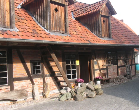 Kastenmangel in Steinhude Historisches Fachwerkhaus mit rotem Ziegeldach, Holzverzierung und farbenfrohen Pflanzen im Vorgarten.