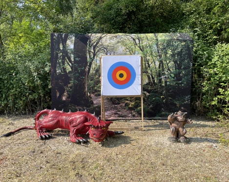 Bogenschule in Erkrath Eine Waldlichtung mit einer Zielscheibe, umgeben von Plastiktiere eines Drachen und eines Affen.