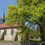 Kirche Münchehagen Historische Kirche mit rotem Ziegeldach und markantem Turm, umgeben von altem Baumbestand.