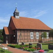 Fachwerk-Kapelle Winzlar Fachwerk-Kapelle mit rotem Ziegeldach und Glockenturm, umgeben von gepflegtem Garten und Grabsteinen.