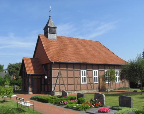 Fachwerk-Kapelle Winzlar Fachwerk-Kapelle mit rotem Ziegeldach und Glockenturm, umgeben von gepflegtem Garten und Grabsteinen.