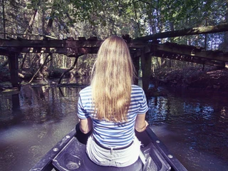 Einfach mal treiben lassen Eine junge Frau sitzt in einem Kanu, treibt auf einem ruhigen Fluss unter einer alten Holzbrücke. Das umgebende dichte Grün vermittelt Ruhe und Gelassenheit.