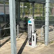 Fahrrad-Reparaturstation Baden Fahrrad-Reparaturstation an einem sonnigen Tag, umgeben von Fahrradständern und Metallzäunen.