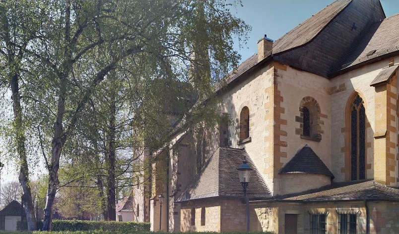 Pfarrkirche St. Laurentius, Clarholz am Kloster Historische Kirche mit romanischen Elementen neben belaubten Bäumen und angrenzenden Gebäuden.