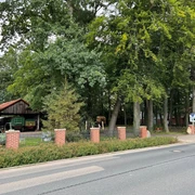 Wohnmobilstellplatz Eystrup Stellplatz mit gepflasterter Zufahrt, umgeben von hohen Bäumen und einer kleinen Holzhütte.