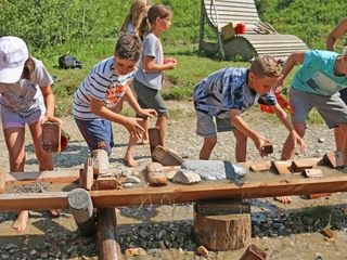 Mit Steinen und Schlamm die Wassermassen stoppen Kinder stauen mit Steinen und Holzelementen Wasser in einem HolzkännelChildren dam up water in a wooden jug with stones and wooden elementsLes enfants utilisent des pierres et des éléments en bois pour retenir l'eau dans un seau en bois.