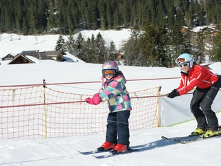 Soon the ski students are riding the rope lift almost alone Kind lässt sich vom Schlepplift hochziehen, die Skilehrerin ist hinter ihmChild is pulled up by the tow lift, the ski instructor is behind himL'enfant se laisse hisser par le téléski, la monitrice de ski est derrière lui