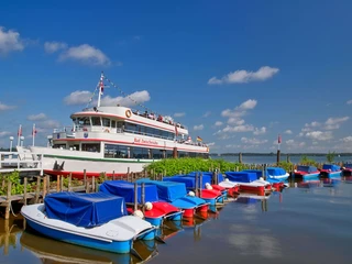 boote-weisse-flotte Ein weißes Ausflugsschiff der Weißen Flotte liegt am Steg, umgeben von farbenfrohen Freizeitbooten.
