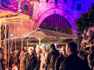 VeedelsAdvent on the Chlodwigplatz Festlich beleuchteter Chlodwigplatz bei Nacht. Die Severinstorburg im Hintergrund erstrahlt in violettem Licht, während zahlreiche Menschen im Vordergrund an einem kleinen Karussell stehen.Festively illuminated Chlodwigplatz at night. The Severinstorburg in the background shines in purple light, while numerous people stand at a small carousel in the foreground.