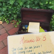 Rätselreise-Wiefelstede-Titelbild Im Vordergrund ein Schild mit der Aufschrift „Hinweis Nr. 5“, im Hintergrund eine geöffnete Schatztruhe.