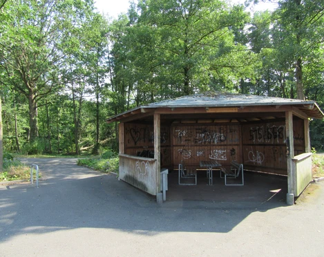 Picknickplatz in der Schutzhütte am Rundweg Nähe Steinhude Bastion 1 Holzhütte mit Graffiti und zwei Bänken auf asphaltiertem Weg im grünen Wald am Rundweg Steinhude.