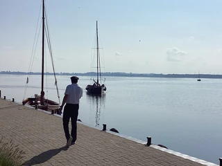 Auswanderer am Anleger Insel Wilhelmstein Ein Mann spaziert auf dem Anleger der Insel Wilhelmstein, während Segelboote auf dem Wasser treiben.